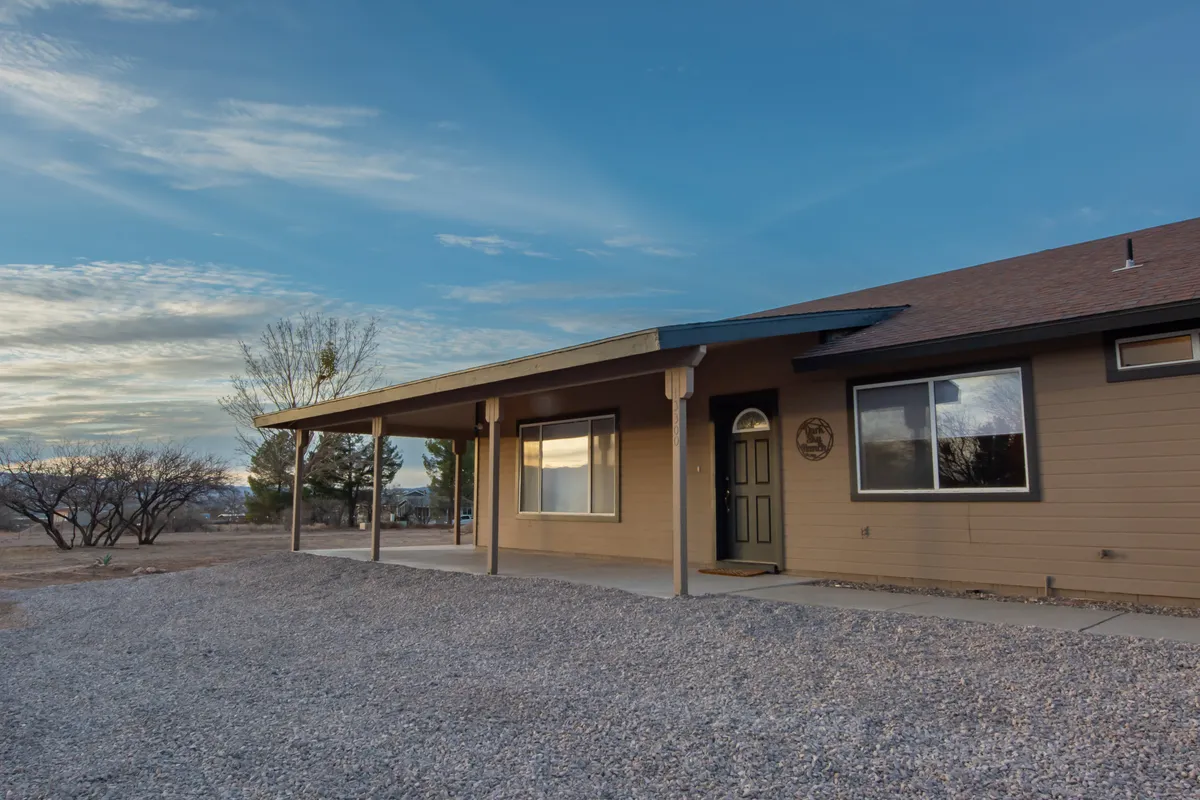 A welcoming exterior view of the home featuring a spacious front porch with large windows and a landscaped gravel area. The porch invites group gatherings, relaxation, and sunset watching, while the yard offers space for outdoor activities.