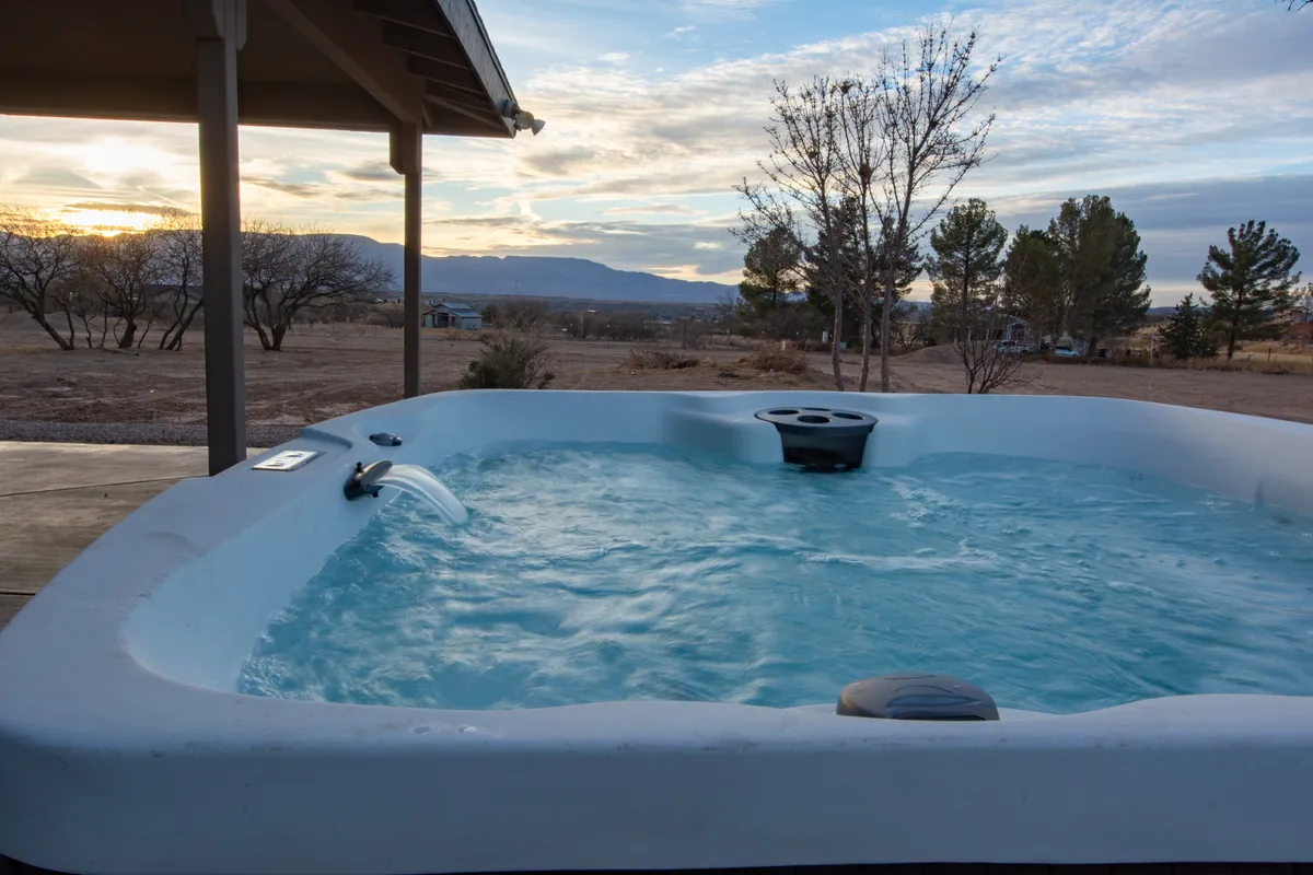A tranquil exterior scene showing a hot tub with a stunning sunset sky and mountains in the background. The setting is peaceful and perfectly captures the idea of soaking in the hot tub while taking in the natural beauty—a popular spot for both romance and wellness.