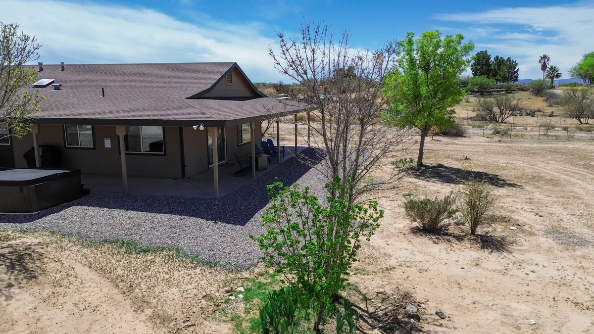 A tranquil exterior shot of the main house and its wraparound porch, surrounded by lush greenery and a gravel pathway. The inviting porch space encourages relaxation, offering the perfect setting for sunset views or a romantic candlelit dinner outdoors.