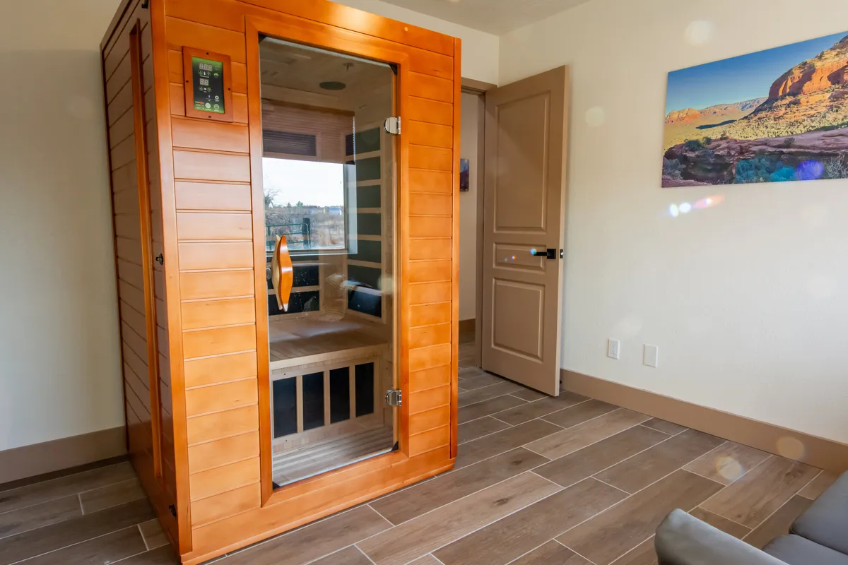 An inviting interior shot of a sauna room with rich wooden textures, a doorway, and curated artwork on the wall. The warm, natural materials evoke a spa-like atmosphere, ideal for wellness sessions and quiet reflection.