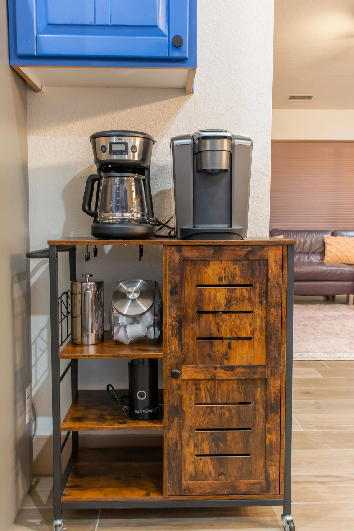 A compact coffee station featuring a Keurig machine and wooden cart, inviting guests to gather for morning coffee or pre-adventure planning. The setup feels warm and communal, suggesting shared moments before setting out to explore.