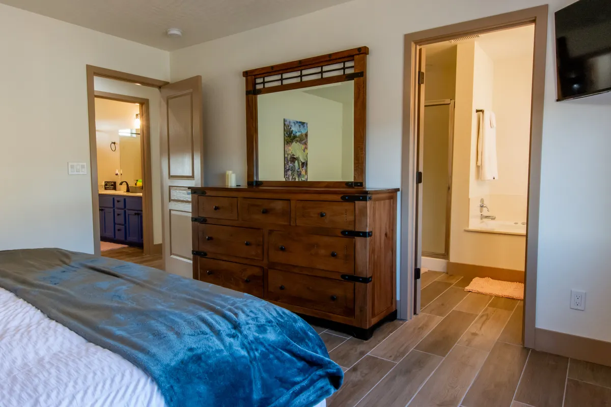 A peaceful corner with a wooden dresser, mirror, and open doorway leading to a bathroom, evoking a sense of preparation and anticipation. The scene sets a tone of relaxed transitions, whether getting ready for a group outing or winding down after a day’s adventure.