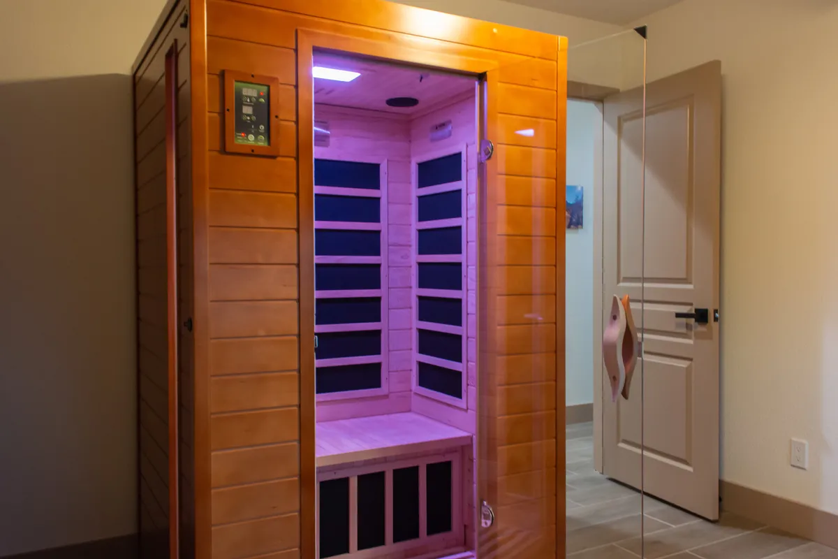 This interior image features an infrared sauna with ambient lighting and a glass door, set within a tranquil and minimalistic space. The soothing glow and modern design create an immediate sense of calm and focus on wellness rituals.