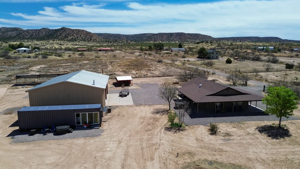 A broad view of the main house and its grounds shows a relaxed outdoor seating area, open landscape, and storage building. The setting looks ready for outdoor activities, social gatherings, or quiet moments with nature. The sky overhead is expansive and clear.