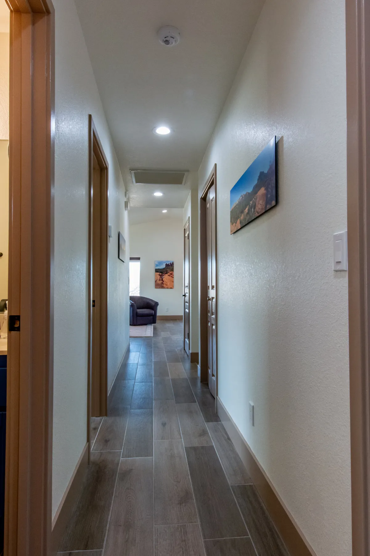 A long, inviting hallway lined with artwork, leading to various rooms with a cozy seating area at the end. The scene evokes movement through the home and gathering points for families or friends.
