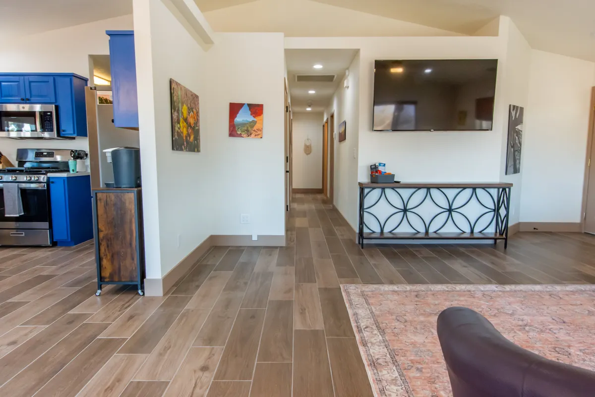 A modern and inviting kitchen and living area featuring blue cabinetry, a large flat-screen TV, decorative artwork, and a stylish console table. The open design is ideal for cooking, entertaining, and sharing quality time with a group.