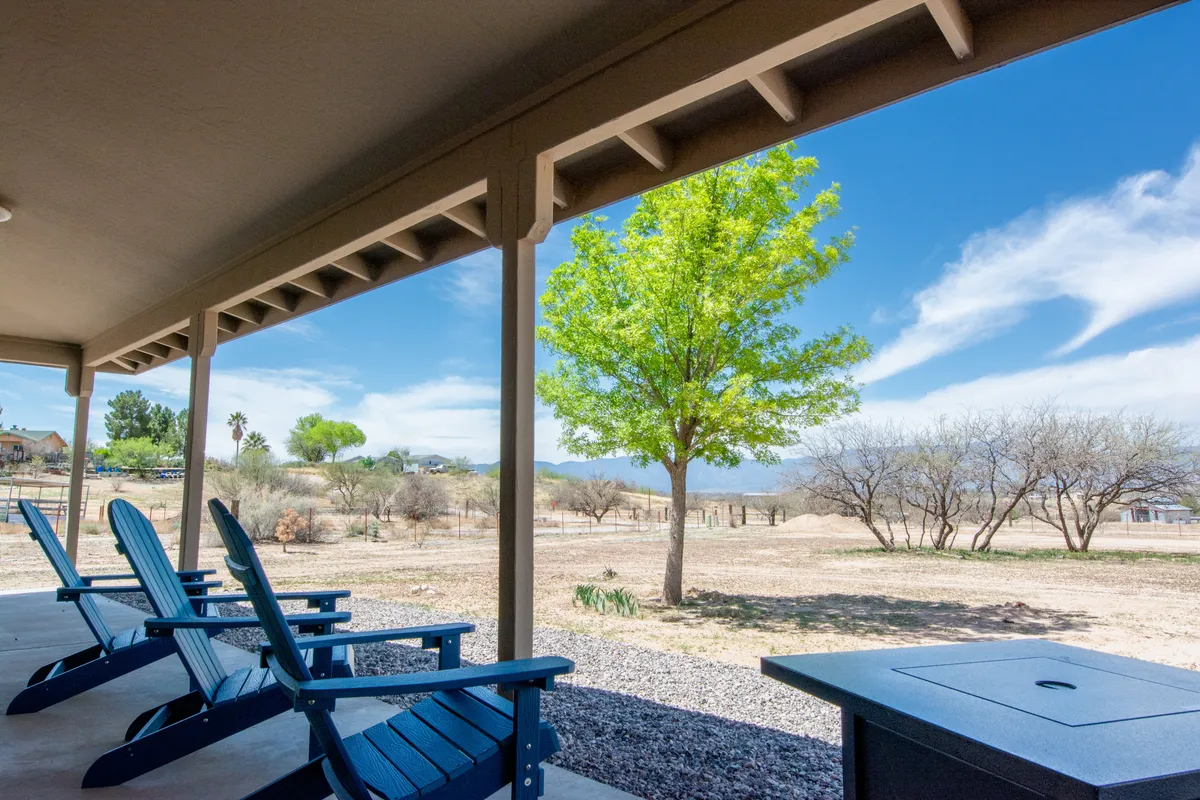 A peaceful outdoor setting featuring adirondack chairs beneath a leafy tree, overlooking an open landscape. The area is ideal for stargazing or sharing a quiet drink as night falls, evoking a sense of seclusion and connection with nature.